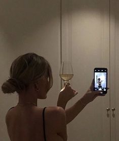 a woman taking a selfie with her cell phone while holding a glass of wine