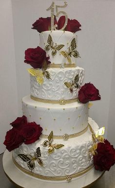 a three tiered wedding cake with red roses and butterflies on the top, sitting on a table