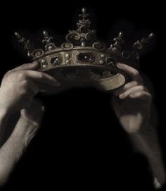 a person holding up a golden crown in the dark, with their hands on it