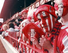 two fans wearing red and white face paint in the stands at a soccer game with their faces painted