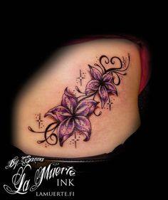 a woman's lower back tattoo with purple flowers and swirls on the side