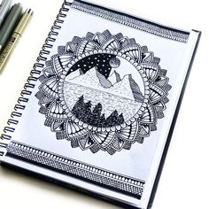 a notebook with an image of mountains and trees in the middle, surrounded by two pens