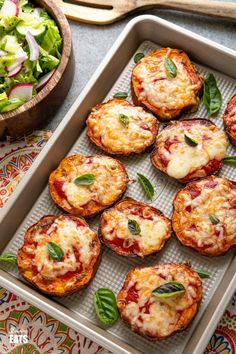 mini pizzas with cheese and spinach are on a tray next to a salad