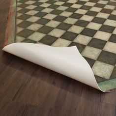 a white piece of paper sitting on top of a wooden floor next to a black and white checkered rug