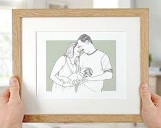 a person holding up a framed drawing of a man and woman in the middle of their hands