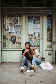 a man and woman sitting on the ground in front of a building with posters behind them