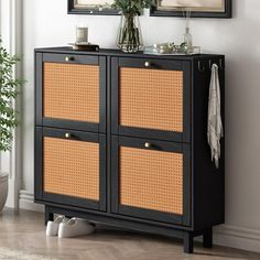 a black cabinet with wicker doors and two framed pictures on the wall above it