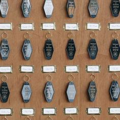 many different types of key chains hanging on a wooden wall with name tags attached to them