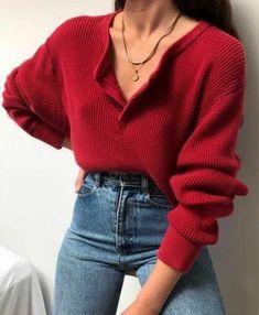 a woman wearing a red sweater and jeans is posing for the camera with her hands on her hips