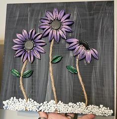 a hand holding up a piece of art made out of paper and flowers on a chalkboard