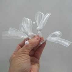 a hand is holding two small white bows with pearls on the ends and ribbon around them