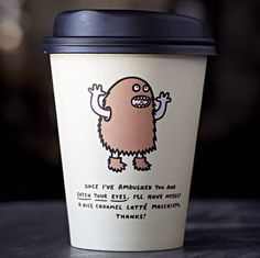 a coffee cup with a cartoon character drawn on the front and side, sitting on a table