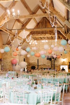 tables and chairs are set up for a wedding reception with paper lanterns hanging from the ceiling