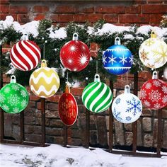 christmas ornaments hanging from a fence in front of a brick wall with snow on it