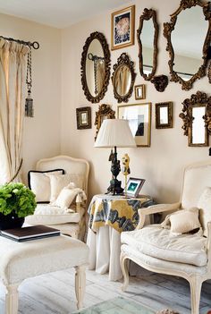 a living room filled with white furniture and lots of mirrors on the wall above it