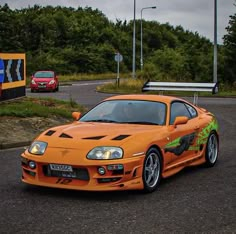 an orange sports car parked on the side of a road next to a parking lot