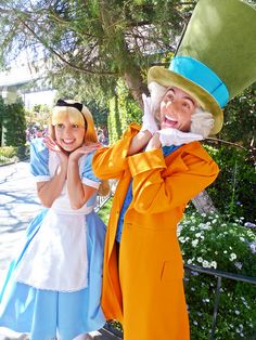 two people dressed in costumes standing next to each other on a sidewalk with trees and bushes behind them