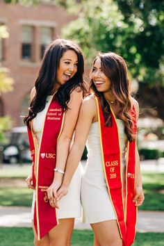 two women in red and yellow graduation gowns standing next to each other on the grass