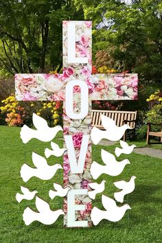 a cross with flowers and doves on it in front of a park bench that says love