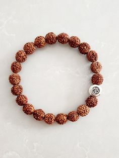 "This stretch bracelet MAKES A GREAT RAKHI FOR RAKSHA BANDHAN It is made with 8mm round rudraksha wood beads and a 9mm round (circle, not sphere) Om bead. Rudraksha refers to a stonefruit. Traditionally, Hindus and Buddhists wore rudraksha beads (bracelets & necklaces) for prayer. However, ANYONE can wear rudraksha beads. Rudraksha is said to help bring harmony in families. It aids in meditation and helps to sanctify one's mind, body and spirit. The \"Om\" symbol signifies oneness with the universe. The word \"Om\" is commonly used as a form of meditation to create peace for the mind, body and soul. Many people who practice yoga and meditation often chant \"om\" to connect the mind, body and soul. This bracelet is made to order. Bracelet length is the inner circumference. For this bracelet Brown Bracelets For Meditation And Festivals, Rudraksha Rakhi, Spiritual Brown Round Stretch Bracelet, Brown Stretch Bracelet For Meditation, Spiritual Brown Stretch Bracelet, Brown Round Spiritual Stretch Bracelet, Rudraksha Breslet For Men, Rudraksha Jewelry Bracelets, 5 Mukhi Rudraksha