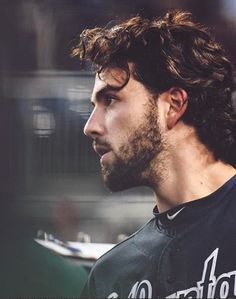 a man with long hair and beard wearing a baseball uniform looking off into the distance