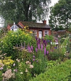 an old brick house surrounded by flowers and greenery in the foreground, next to a garden