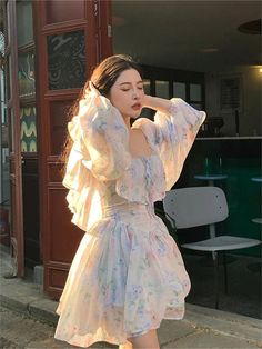 a woman standing on the sidewalk wearing a white dress with floral print and puffy sleeves