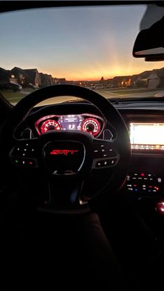 the interior of a car with dashboard lights and steering wheel controls at sunset or dawn