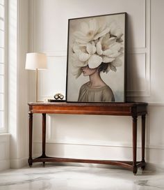 a table with a painting on it next to a lamp and a framed photograph in the corner