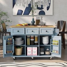 a blue kitchen island with lots of plates and bowls on it's sides, in front of a painting