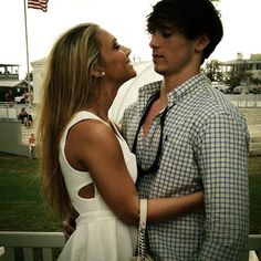 a young man and woman standing next to each other in front of a flag pole