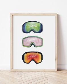 three pairs of ski goggles are displayed in a wooden frame on the floor next to a wall