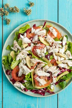 a salad with tomatoes, lettuce and chicken on a blue wooden table top