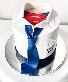 a superman shirt and tie on top of a white cake with blue ribbon around it