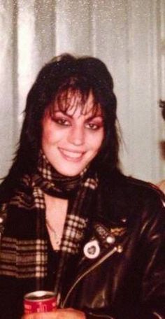 a woman in a leather jacket holding a can of soda and smiling at the camera