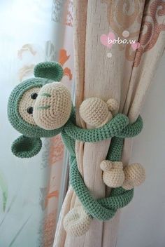 a crocheted monkey hanging from the side of a curtain rod in front of a window