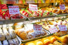 many different types of pastries on display in a bakery case with price signs for each one