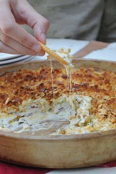 a person is dipping some food into a dish with cheese and sauce on it while sitting at a table