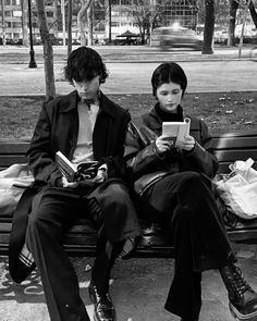 two people sitting on a park bench using electronic devices