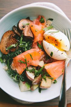 a white bowl filled with food on top of a wooden table next to a fork