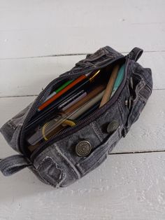 an open purse sitting on top of a white wooden floor with pencils and pens in it