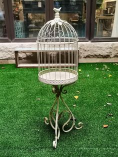 a white birdcage sitting on top of a green grass covered floor next to a window