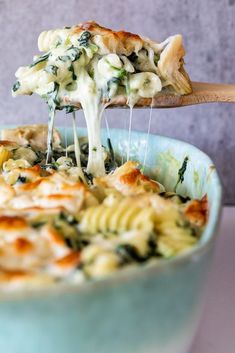 a wooden spoon scooping some pasta out of a blue bowl with spinach and cheese