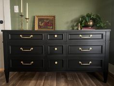 a black dresser with gold handles and knobs in a green walled room next to a door