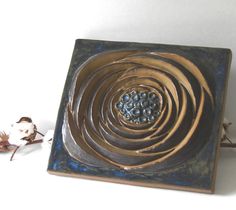 a square metal object sitting on top of a white table next to dried flowers and leaves