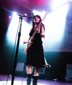 a woman standing in front of a microphone while holding a guitar and wearing knee high boots