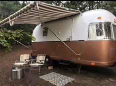 an rv is parked in the woods with its awning open and chairs around it