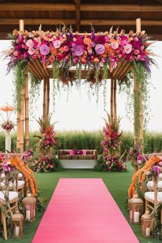 an outdoor ceremony setup with pink and orange flowers on the aisle, white chair covers, and greenery