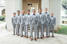 a group of men standing next to each other in front of a building wearing gray suits and bow ties