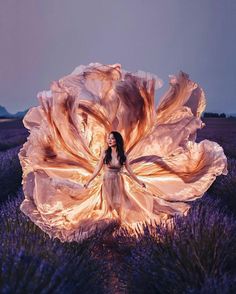 a woman standing in a lavender field with her dress blowing in the wind